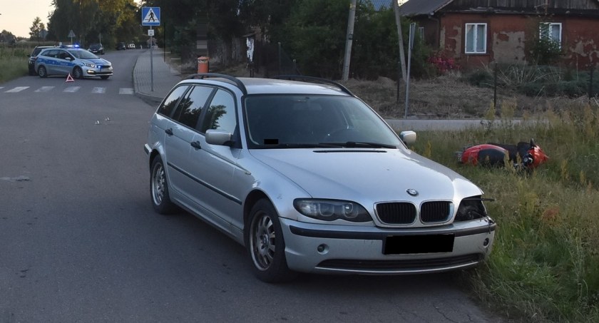 Miejsce wypadku drogowego Samochód BMW stoi na jezdni. Motorower leży na trawiastym poboczu