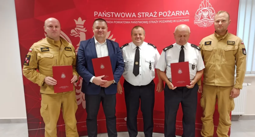 Fotografie dokumentujące historyczne podpisanie porozumienia między PSP, OSP Fiukówka i Wójtem Gminy Krzywda w Łukowie. Ważny krok dla zwiększenia bezpieczeństwa mieszkańców poprzez włączenie jednostki do KSRG na kolejne pięć lat. Zobacz jakie osobistości uczestniczyły w ceremonii i jakie symboliczne gesty były częścią tego wydarzenia.